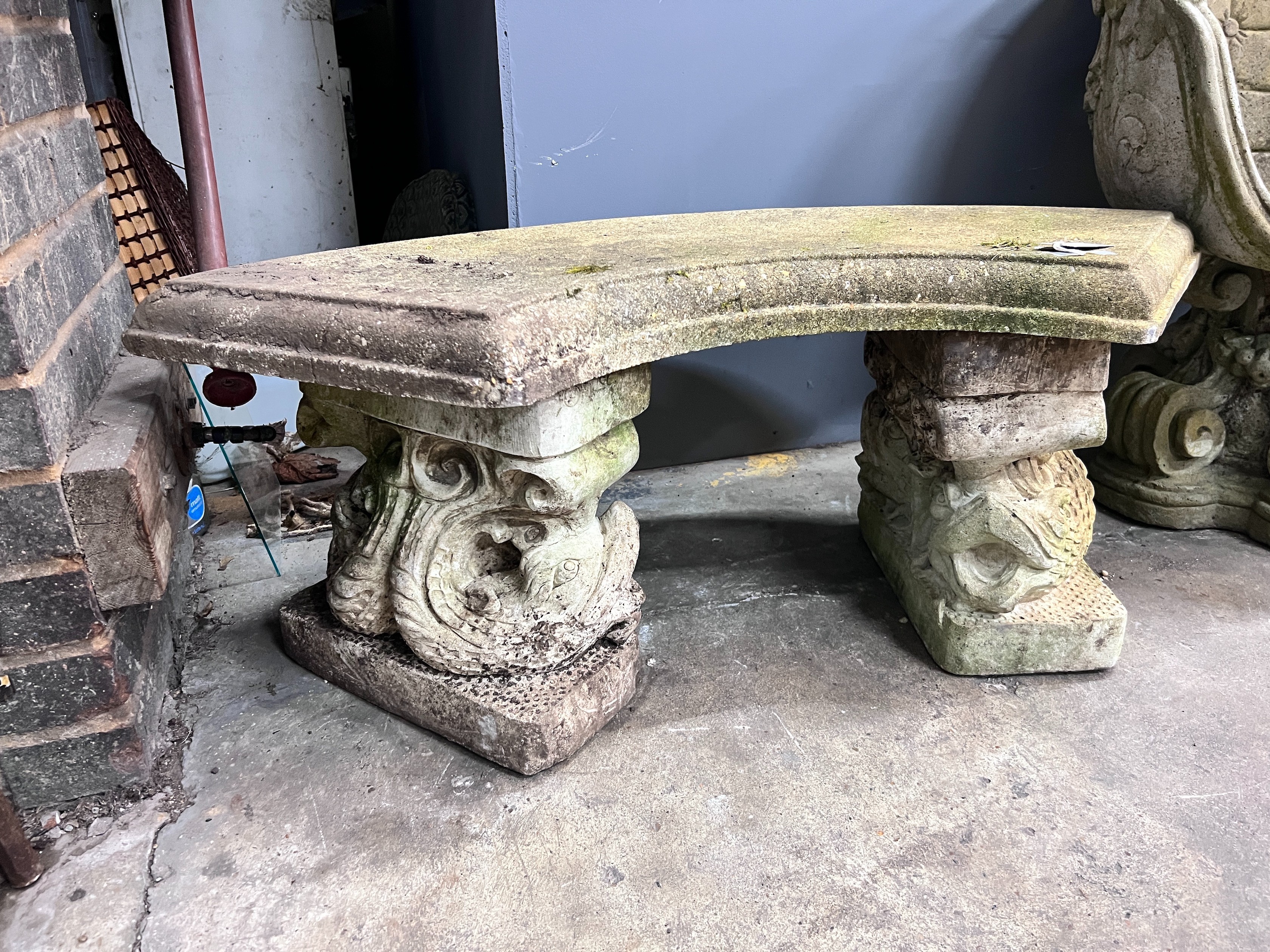 A reconstituted stone curved garden bench with dolphin supports, length 98cm, depth 46cm, height 43cm *Please note the sale commences at 9am.